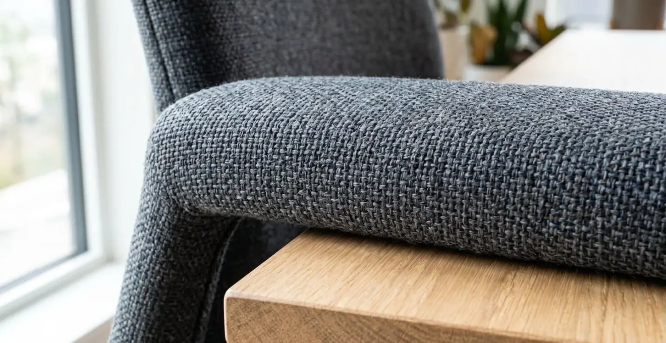 Gros plan macro sur le tissu technique haute densité d'un accoudoir de fauteuil de bureau contemporain, texture de tissage visible, finition mate, bord d'un plateau de bureau en bois naturel net en arrière-plan